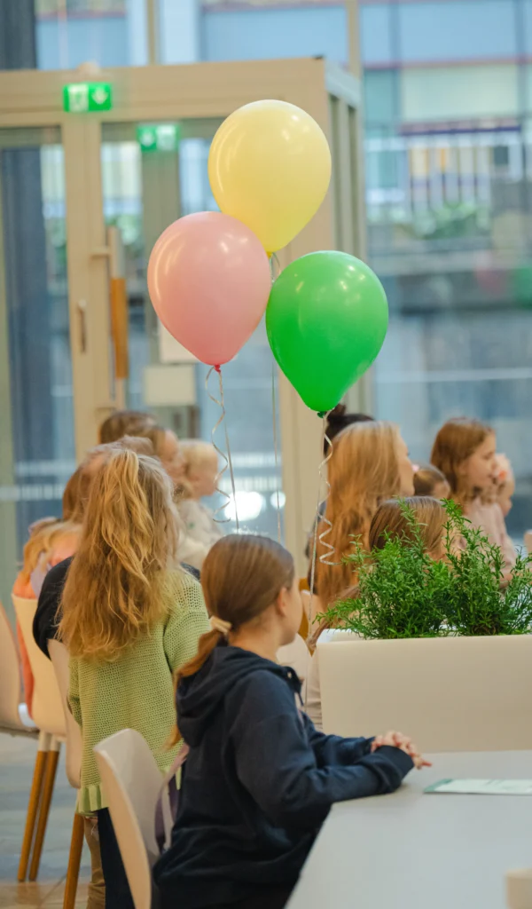 Lapsia istumassa pöydän ääressä sekä ilmapalloja